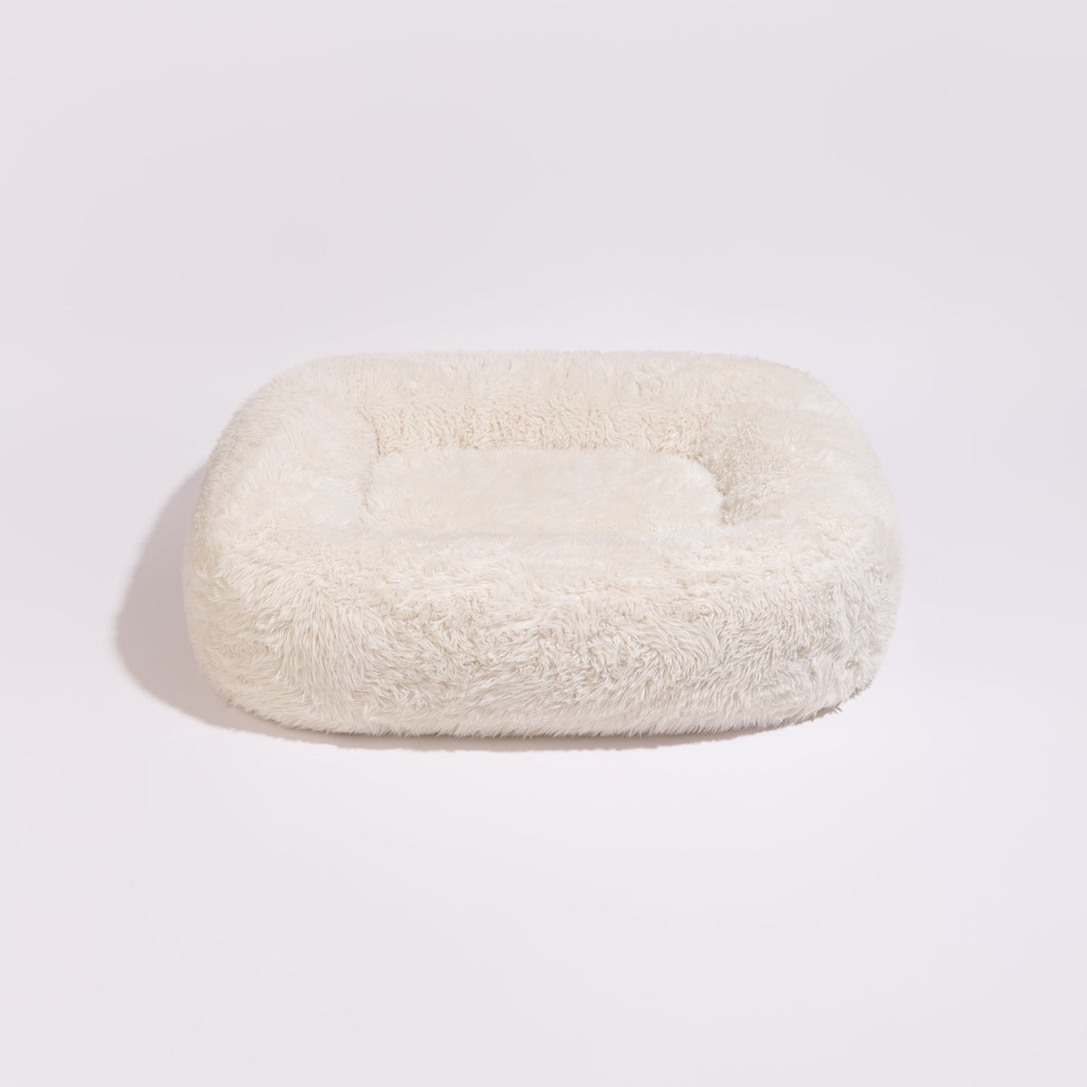 Vaalea Pillow Villa Pebble Flokati -koiranpeti pörröisellä päällisellä ja reunuksilla.